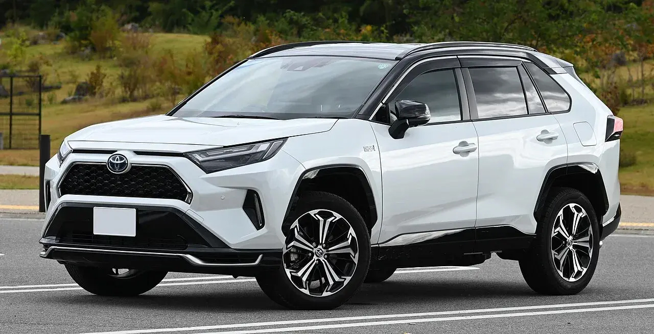 White Toyota SUV parked in a lot, featuring a modern design with black accents and prominent wheels. Trees and grass are visible in the background.