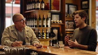 Two men sit at a bar counter engaged in conversation, with drinks and bottles visible in the background, discussing innovations from OpenAI and design inspirations by Jony Ive.