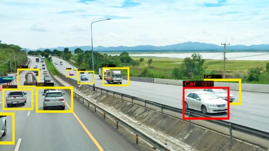 A highway with several cars and trucks labeled in colored boxes, bordered by greenery and a body of water under a cloudy sky.